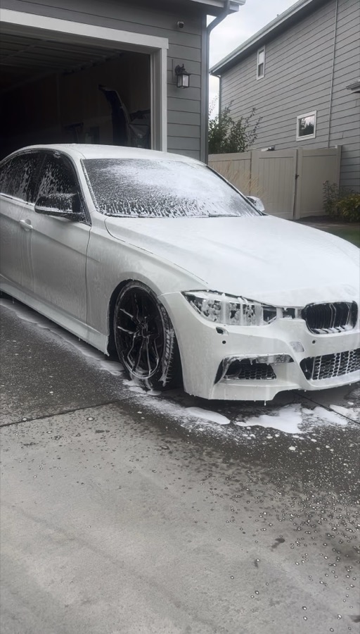 A BMW 3-Series covered in thick wash foam in a driveway